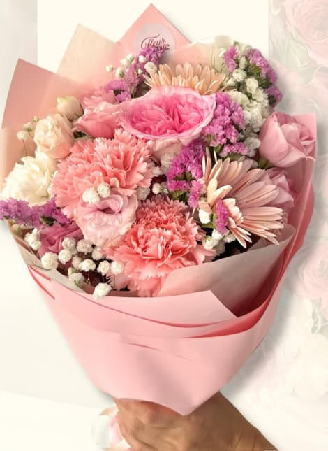 Dense pink bouquet of carnations, roses, and gerbera daisies in pink wrap