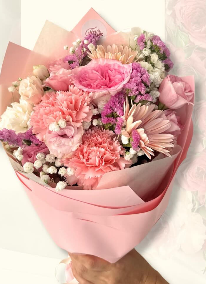 Dense pink bouquet of carnations, roses, and gerbera daisies in pink wrap