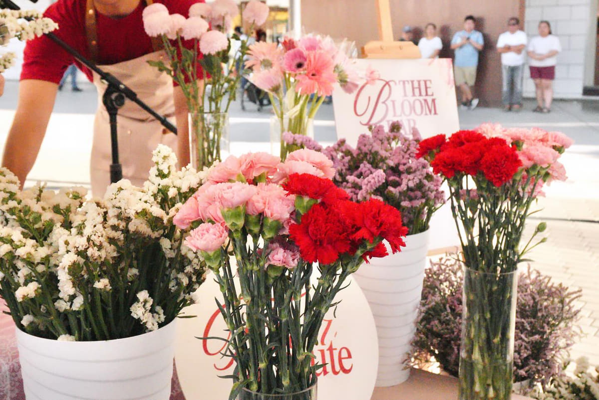 The Bloom Bar easel sign beside buckets of pink carnations and white roses at a pop-up